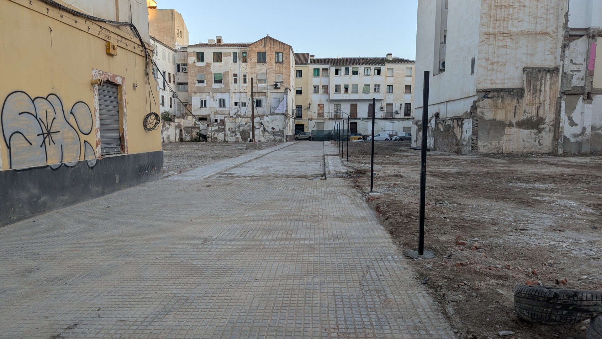 En la foto se aprecia una calle peatonalizada en su tramo final, más próximo al fotógrafo, completamente vacía y bloqueada al paso, tras la demolición de los bloques que suponían la gran mayoría de sus laterales. En el lateral derecho hay unos postes clavados en el suelo previsiblemente para colocar una valla de protección, en el izquierdo, donde todavía sobreviven un par de edificaciones en las esquinas, hay un poste de la luz sobre un bloque de hormigón. Todo el fondo de la imagen lo ocupa un edificio que, al igual que la mayoría de los que se ven en la imagen, es muy antiguo y acumula años de negligencia y abandono.