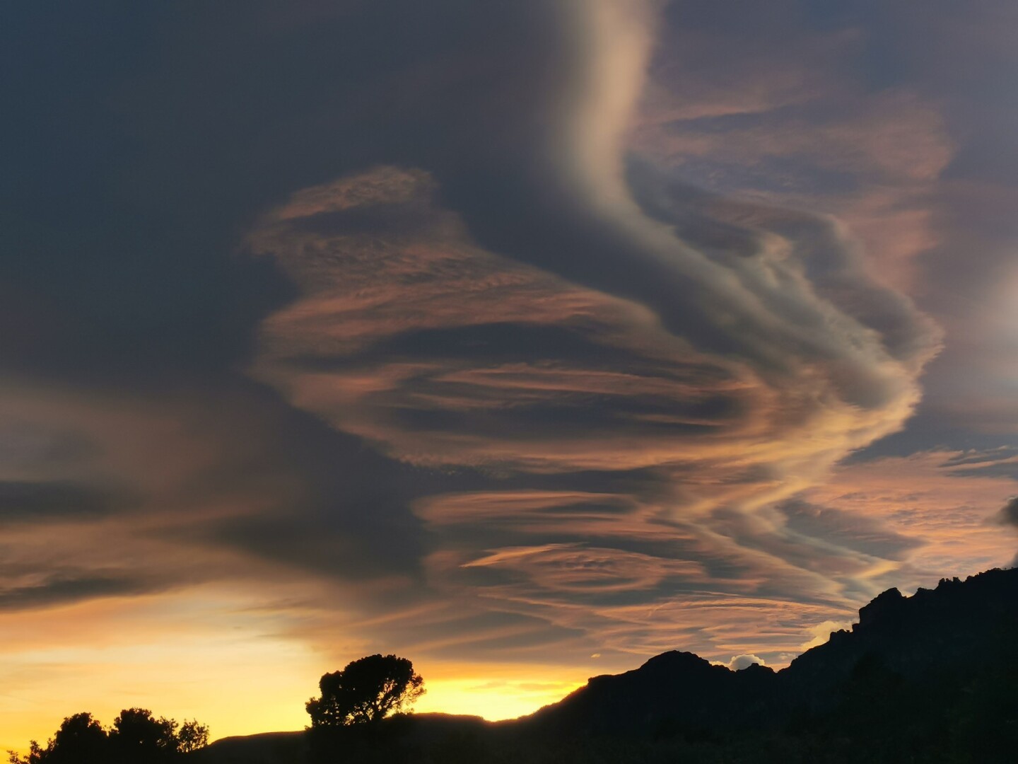 Nubes de viento. Cumulonimbus al atardecer sobre un perfil a contraluz de montañas y arboles en negro. Els Ports del Mont Caro.